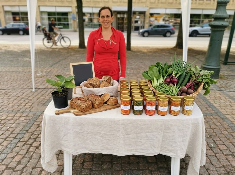 Céline vid La Vie Naturelles marknadsbord med kimchi, glutenfria bröd och en korg grönsaker